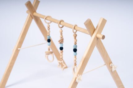 Стилна бебешка гимнастика Leg&Go от естествено дърво с три висящи сензорни играчки в меки сини и неутрални тонове. Насърчава зрителното възприятие, двигателната активност и любопитството на бебето още от първите месеци.